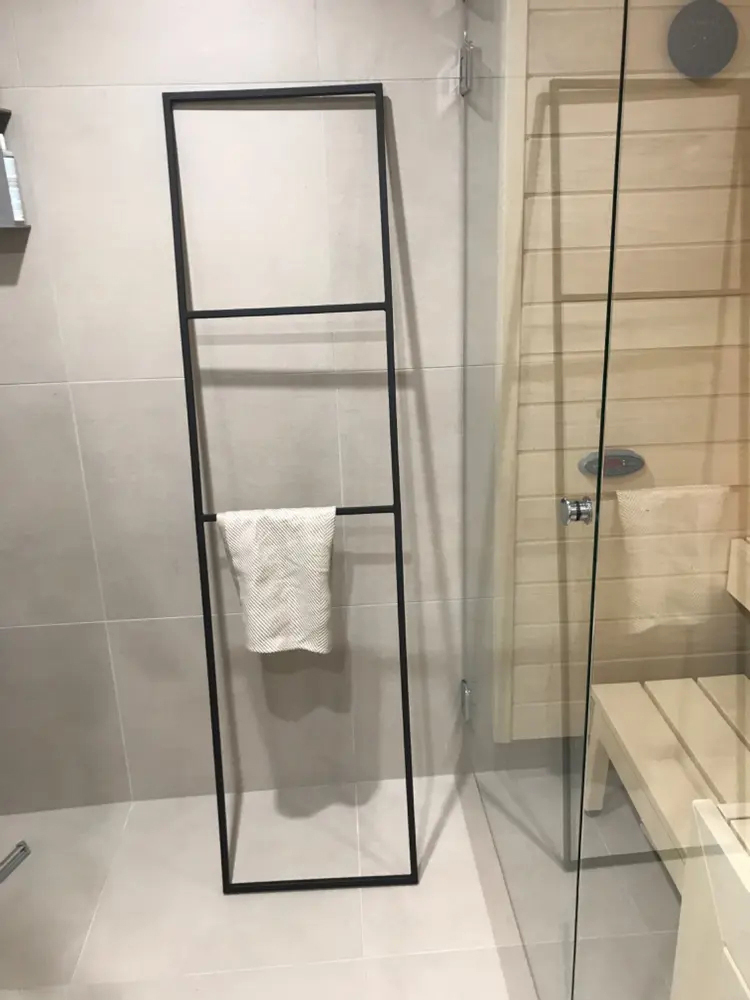 Чёрный каркас Towel для полотенец рядом со стеклянной перегородкой.